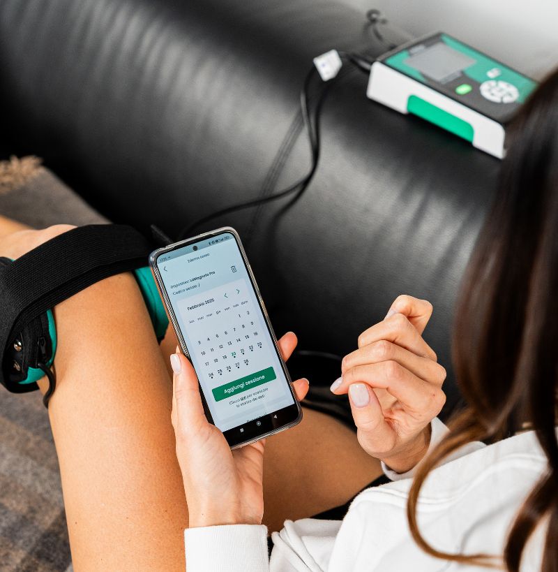 Woman on the sofa doing Magnetotherapy on her knee with LaMagneto Pro. She is using I-Tech Life app to monitor her therapy